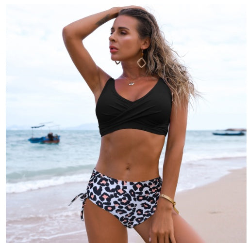 Woman in a black top and leopard print shorts on a beach with boats in the background