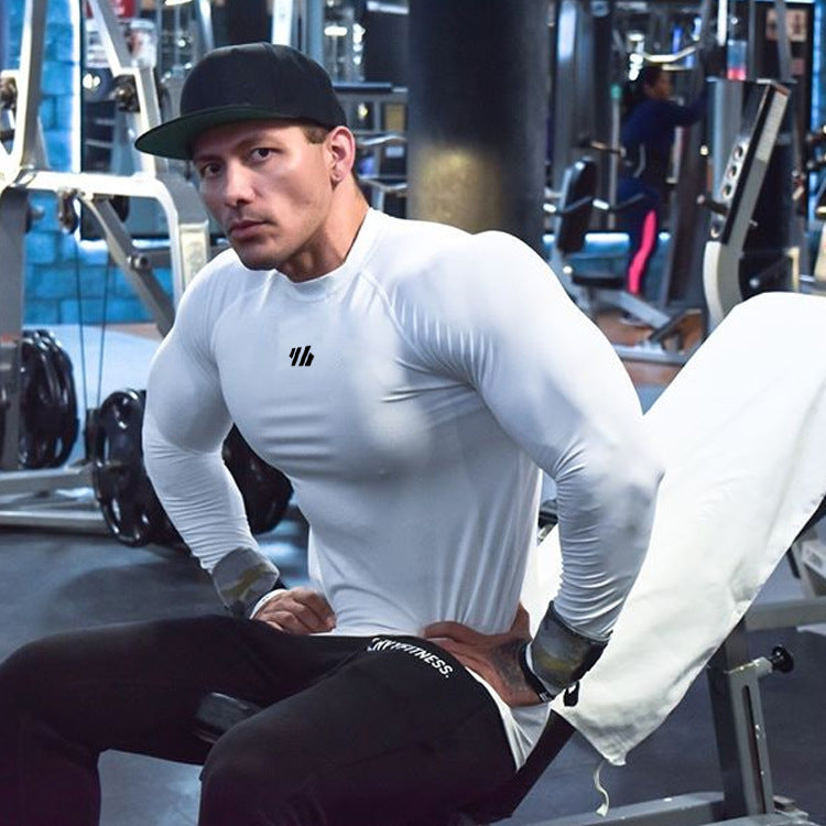 Man in a gym wearing a white long-sleeve shirt with a logo and black pants.