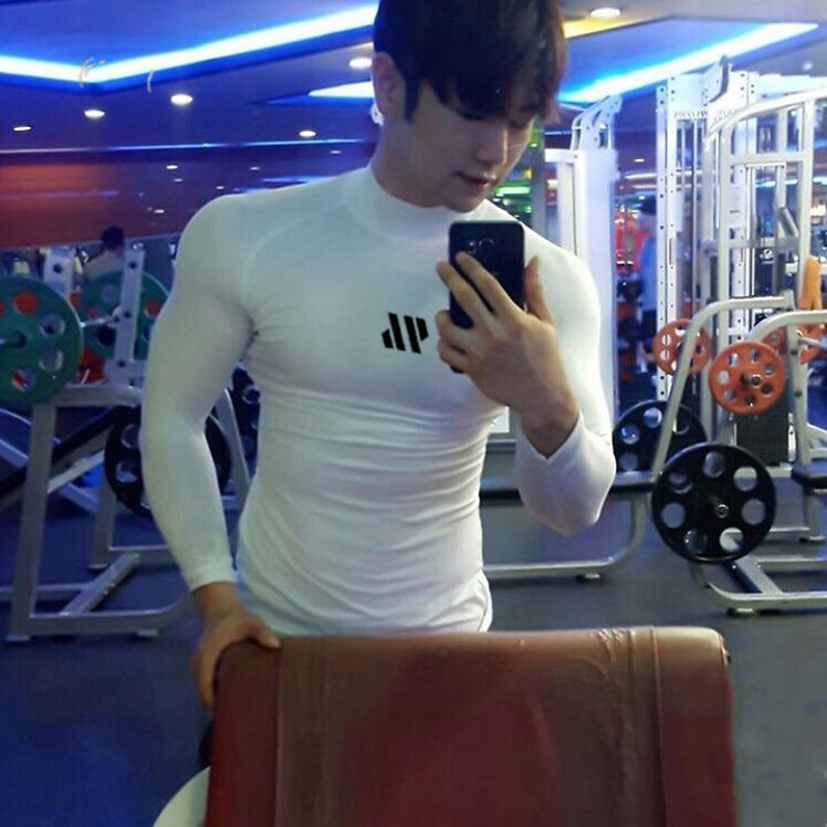 Person taking a mirror selfie in a gym wearing a white long-sleeve shirt.