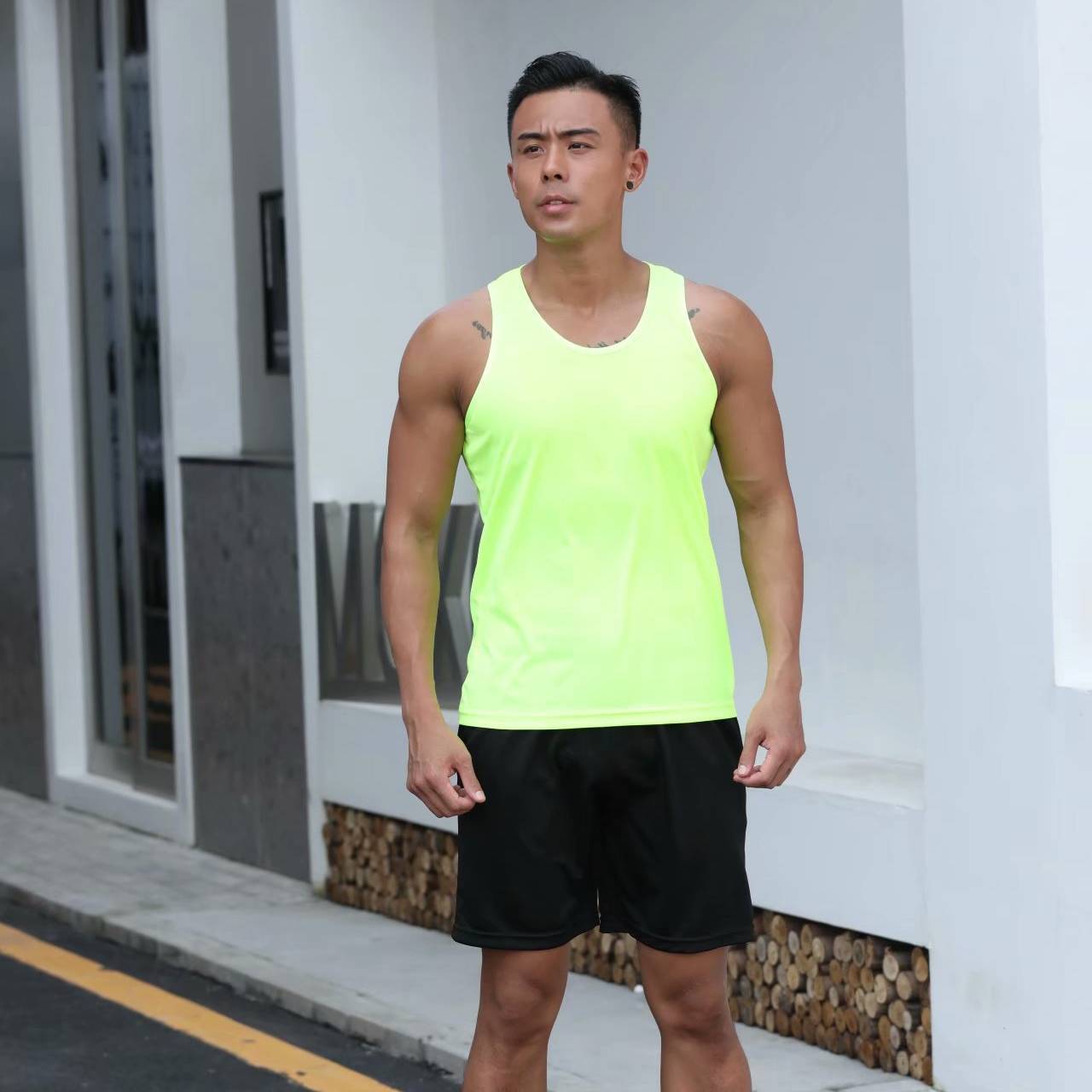 Man wearing a bright green tank top and black shorts standing on a street.