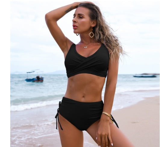 Woman in a black bikini standing on a beach with boats in the background