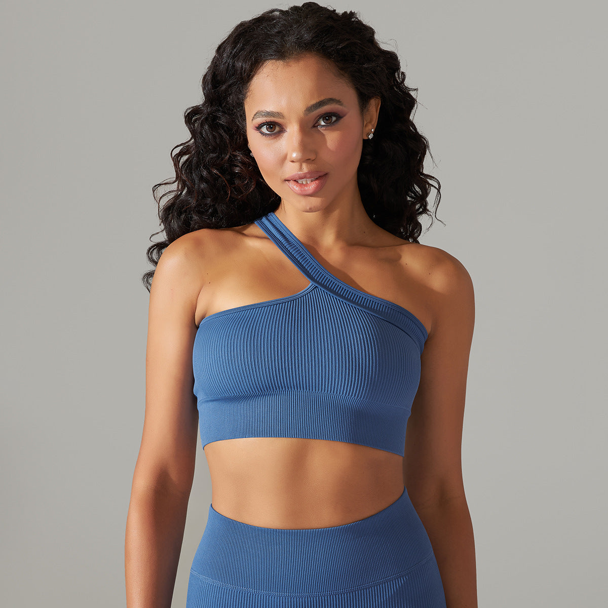Woman wearing a blue one-shoulder top against a gray background