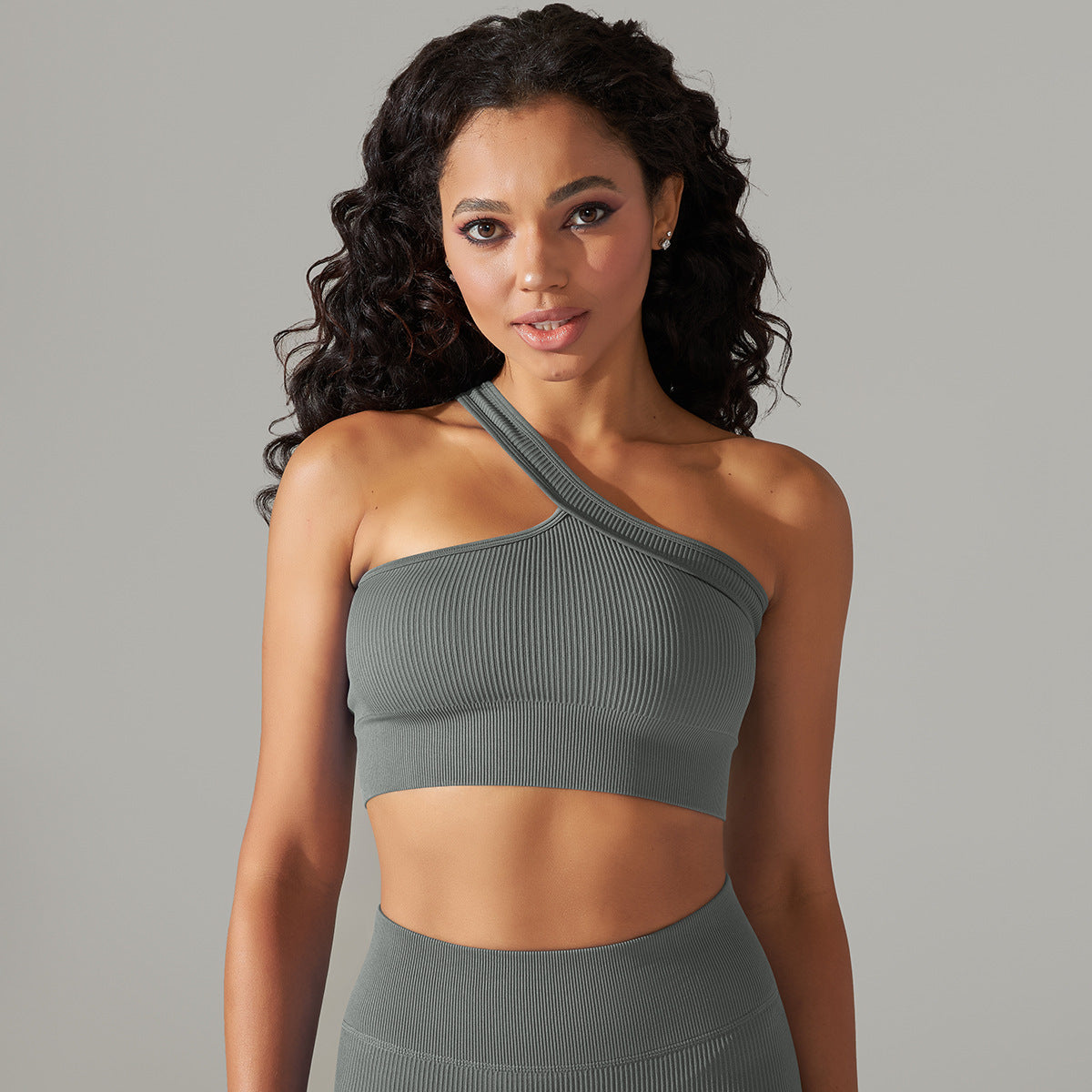Woman wearing a gray one-shoulder top against a gray background