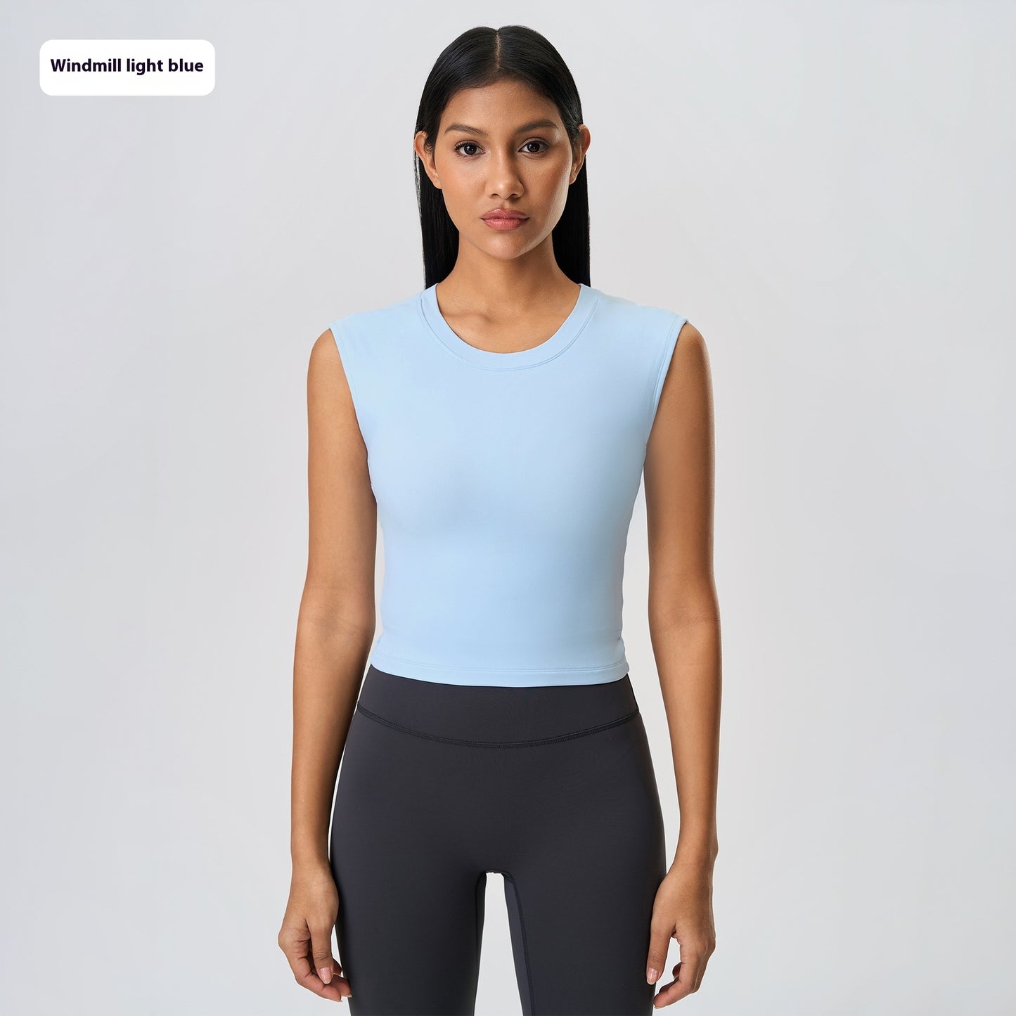 Woman wearing a light blue sleeveless top and black leggings on a gray background