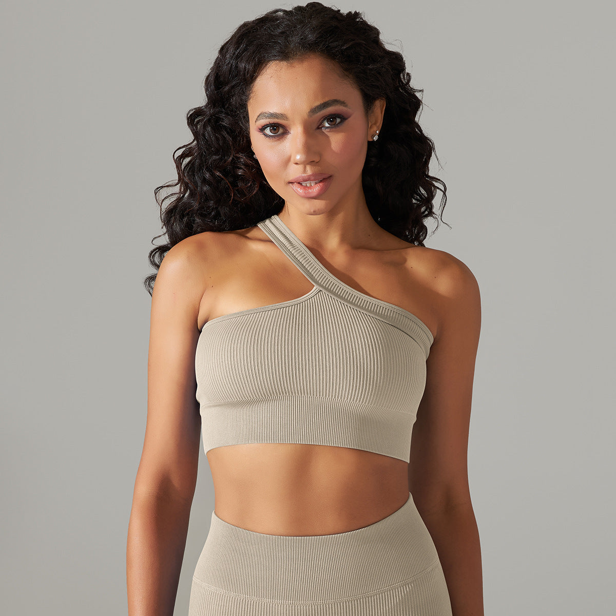 Woman wearing a beige one-shoulder top against a gray background