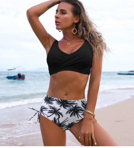 Woman in a black bikini top and palm tree patterned shorts on a beach.