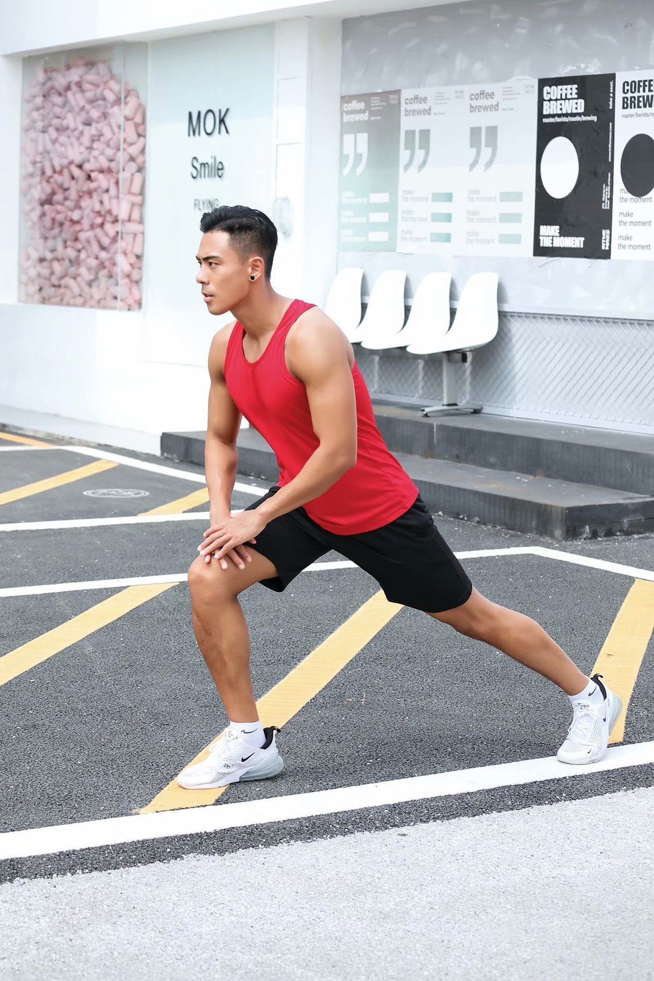 Person in red tank top and black shorts stretching on a street.