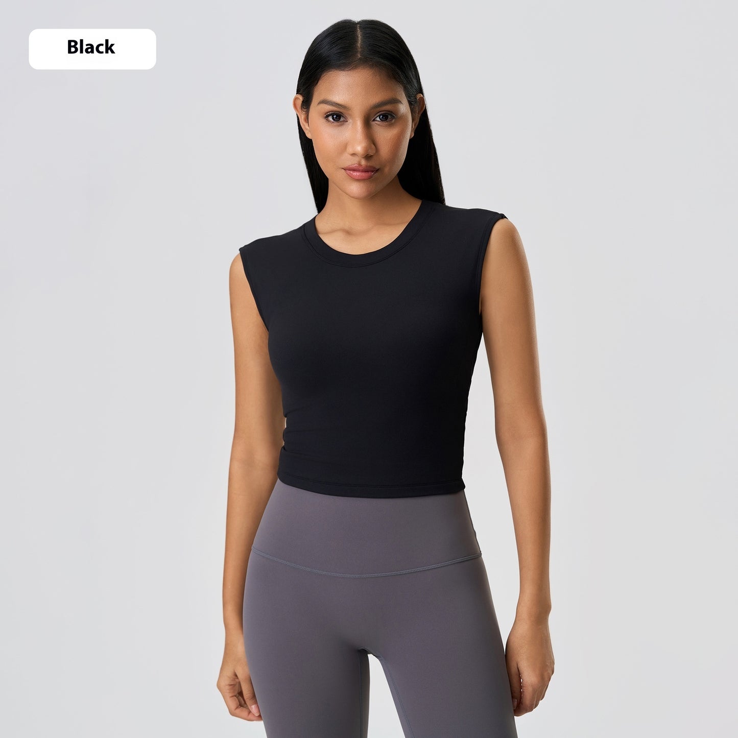 Woman wearing a black sleeveless top and gray leggings on a light gray background