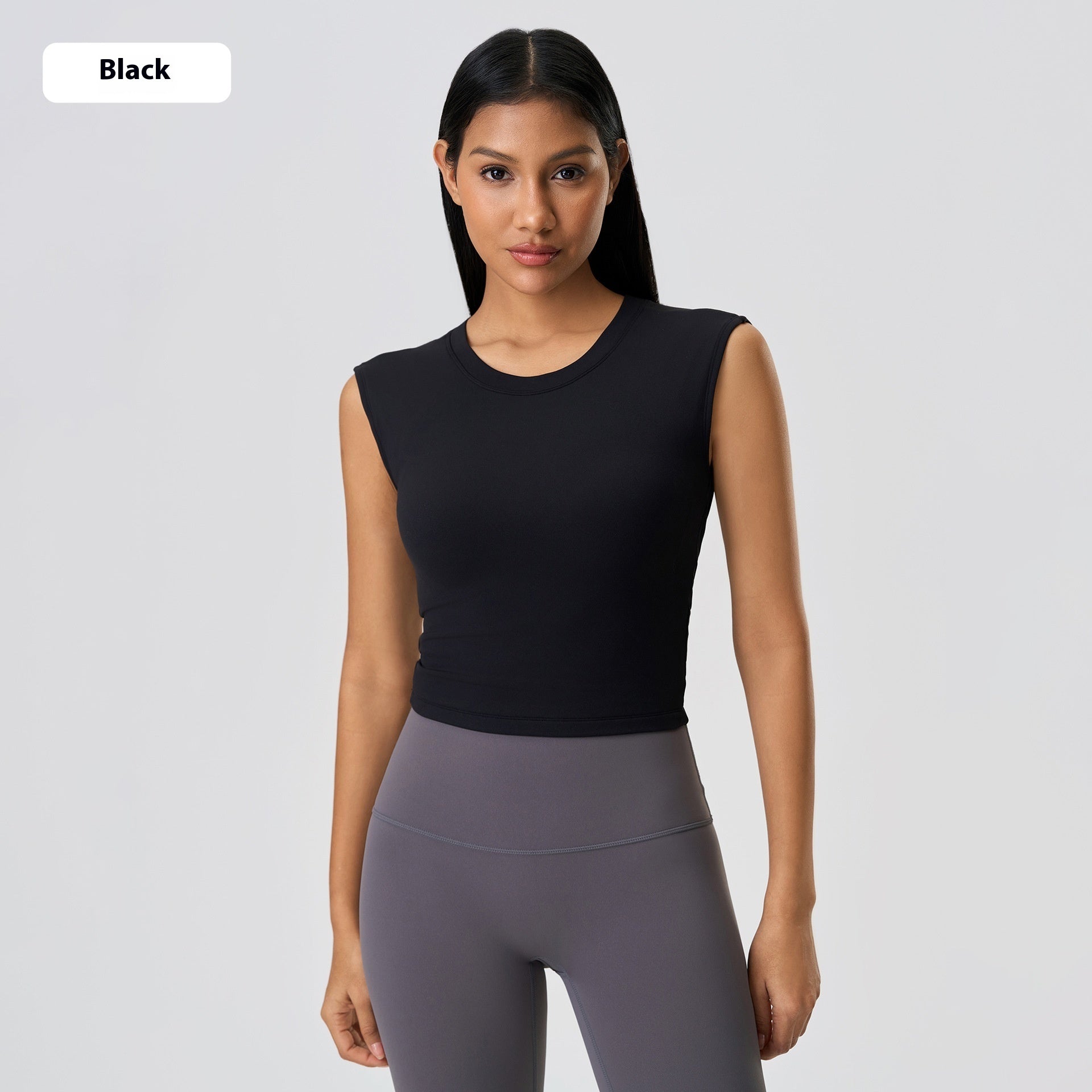 Woman wearing a black sleeveless top and gray leggings on a light gray background