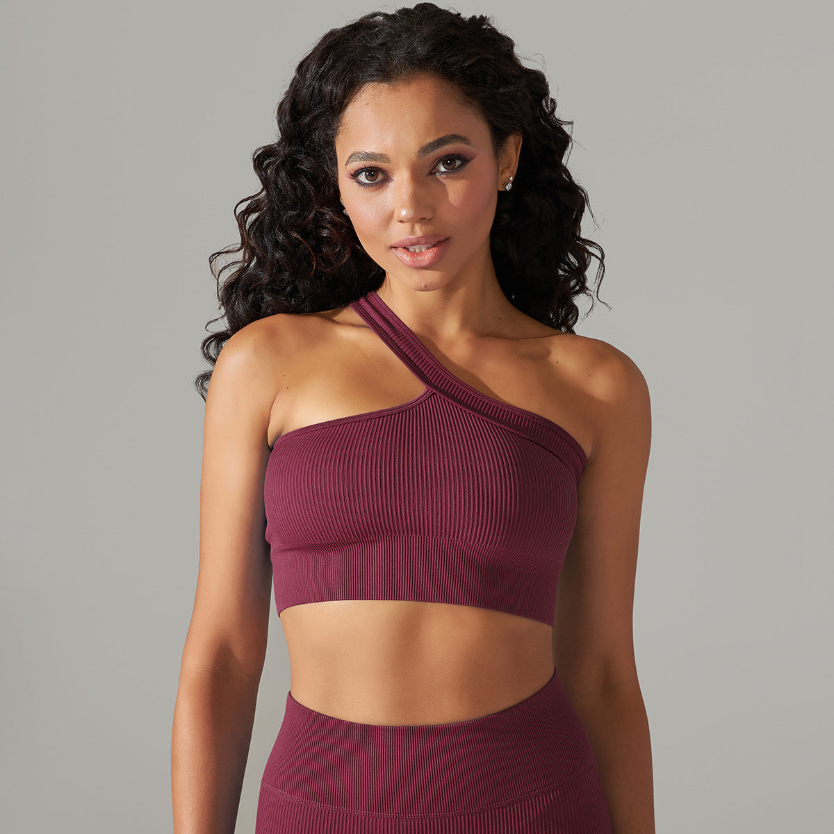 Woman wearing a maroon one-shoulder top and skirt against a gray background