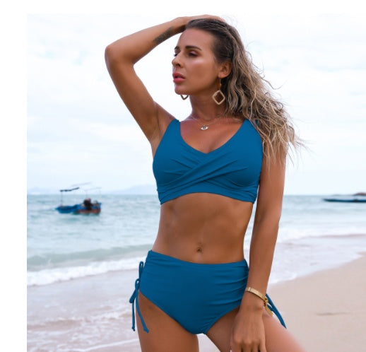 Woman in a blue bikini standing on a beach with ocean and boat in the background