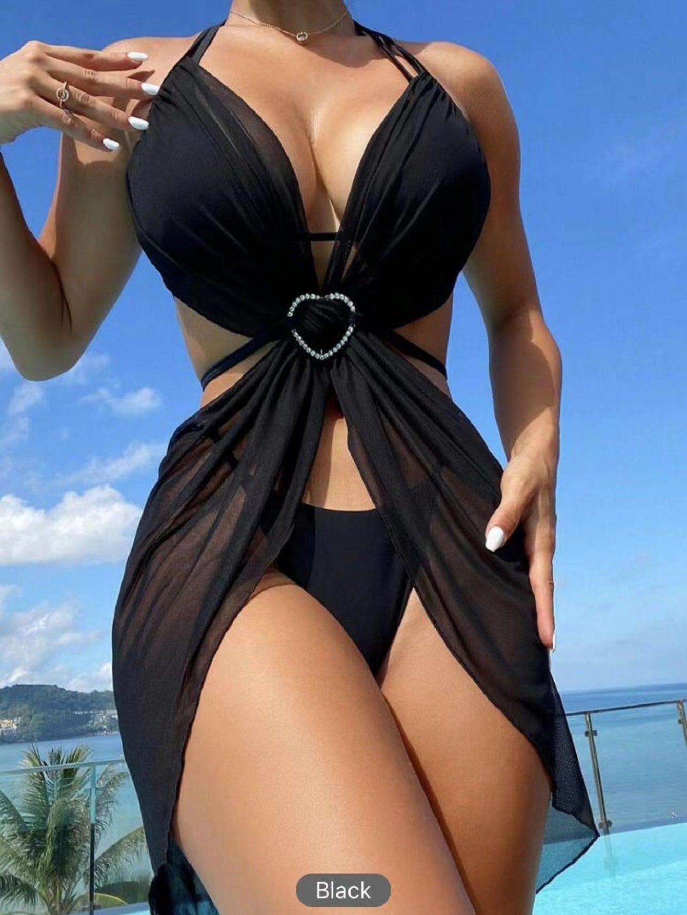 Black swimsuit with a heart-shaped clasp against a blue sky and ocean background